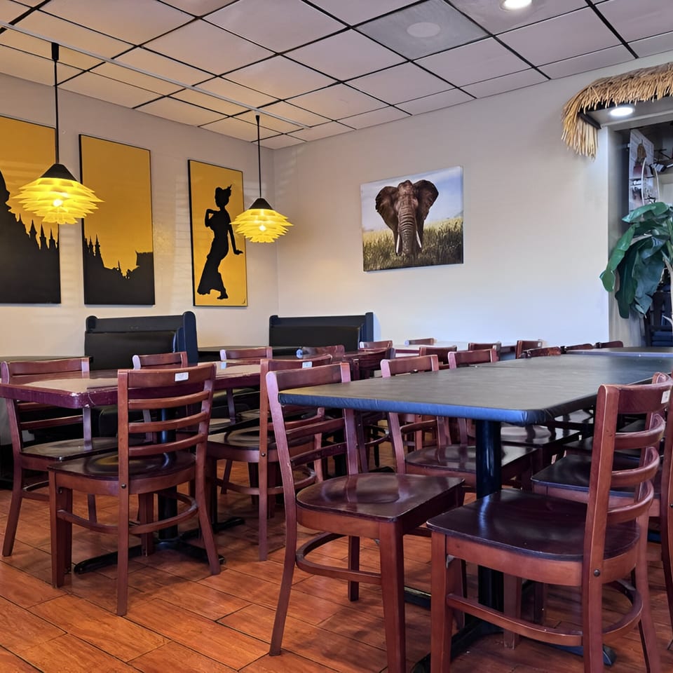 Interior of Lan Xang Thai restaurant with tables, chairs, and Thai-themed artwork on the walls.