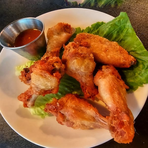 Crispy fried chicken wings on a bed of lettuce with a side of sweet chili dipping sauce.