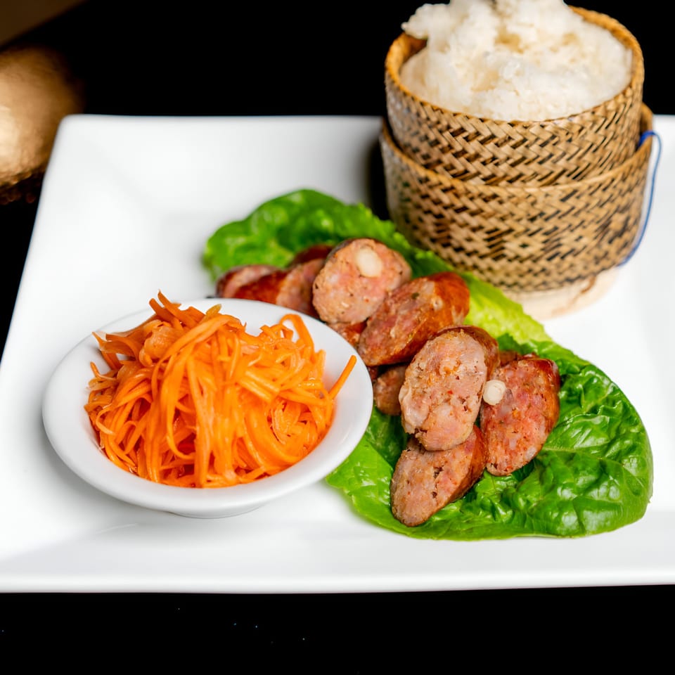 Lan Xang Thai sausage with lettuce, shredded carrots, and sticky rice in a bamboo basket.