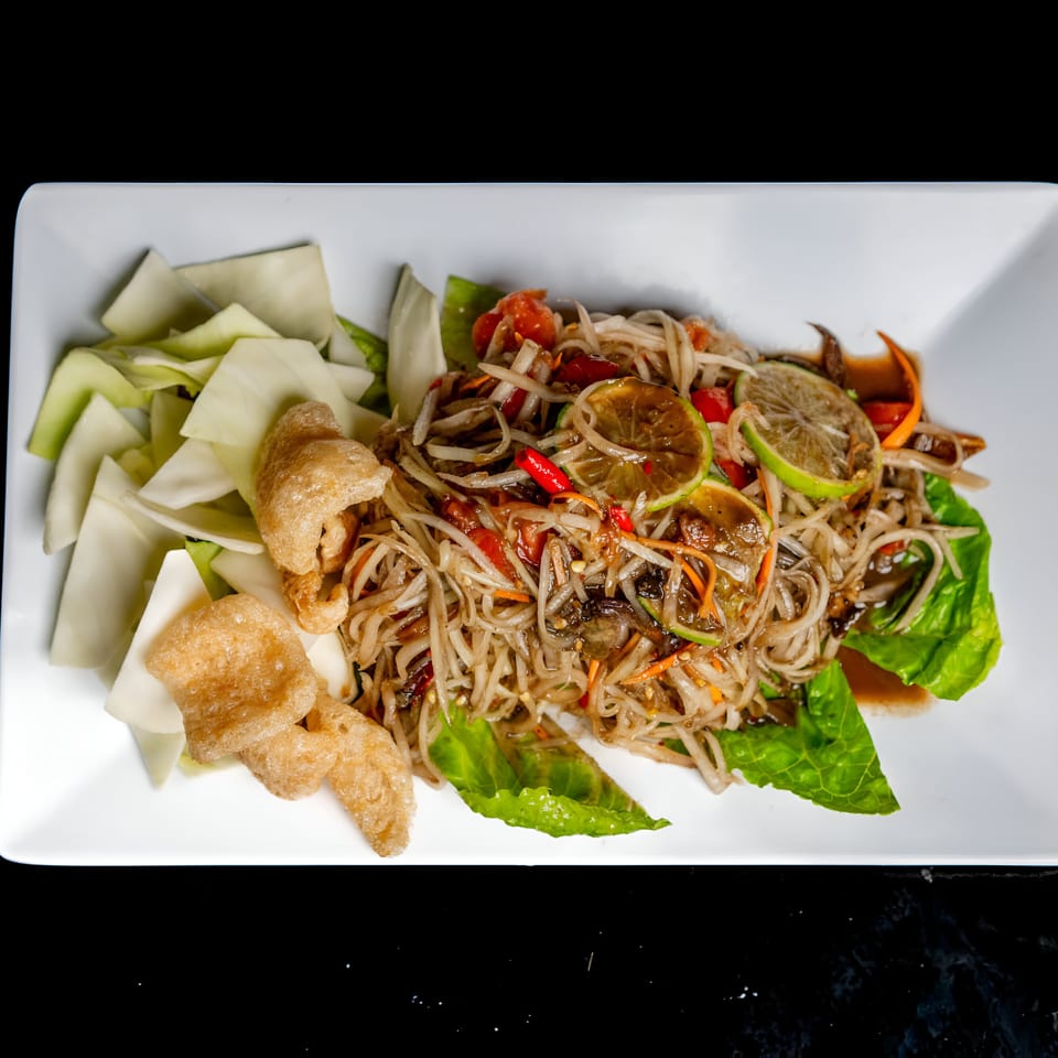 Lan Xang's Thai papaya salad with lime, chili, and pork rinds on a white rectangular plate.