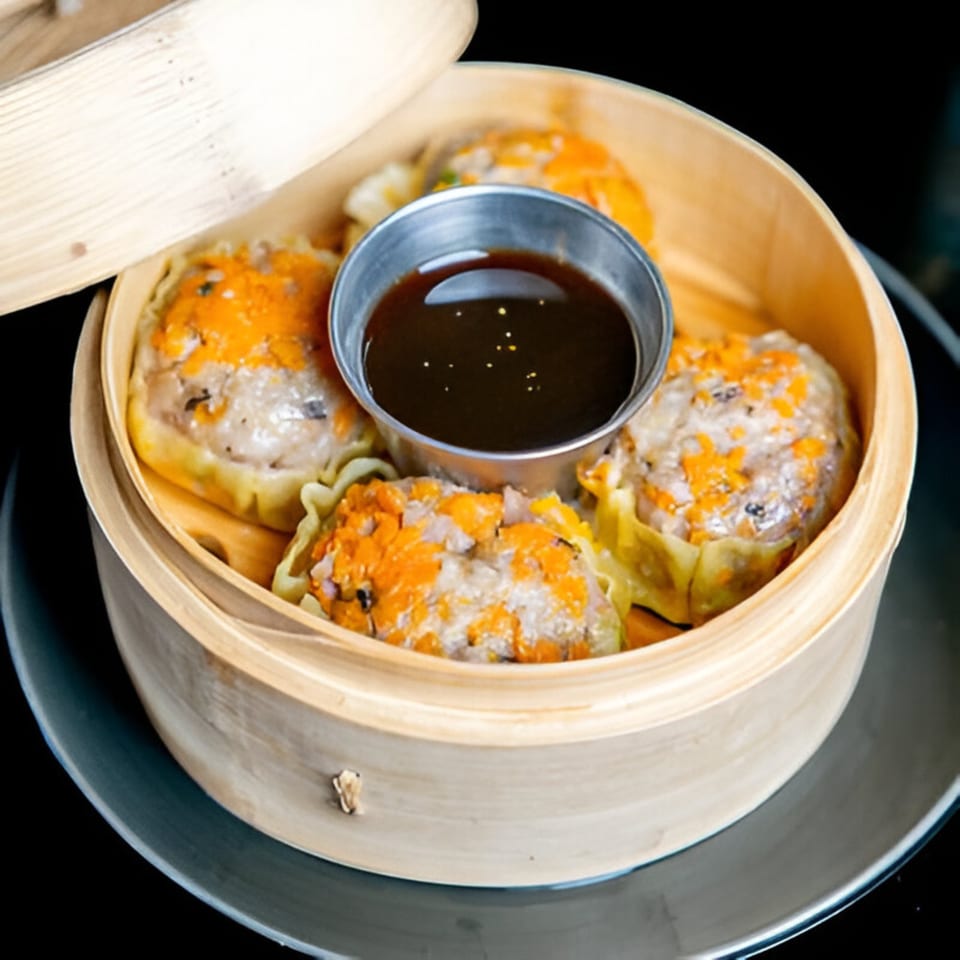 Steamed dumplings with orange roe and a dipping sauce in a bamboo steamer.