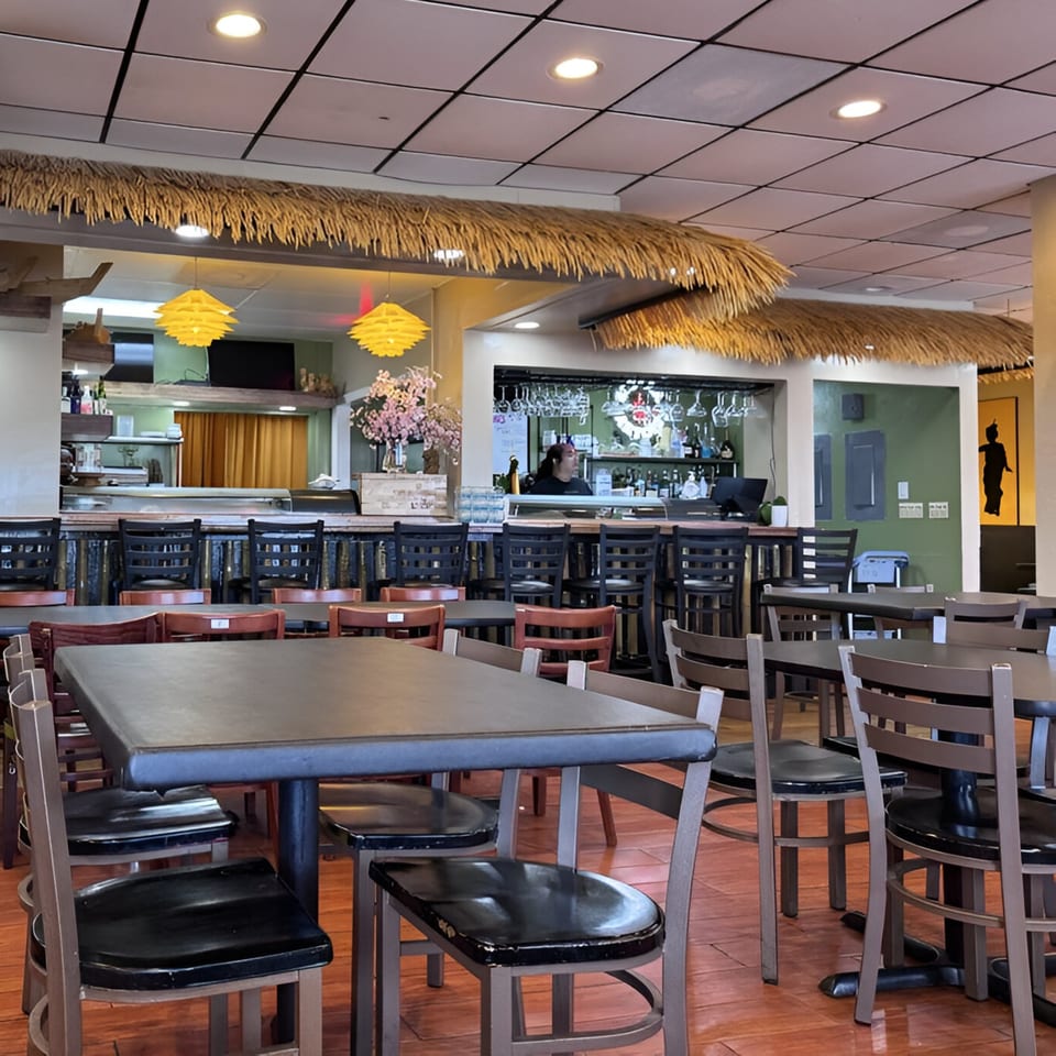 Interior of Lan Xang Thai restaurant with empty tables, chairs, and a bar area with a bartender.